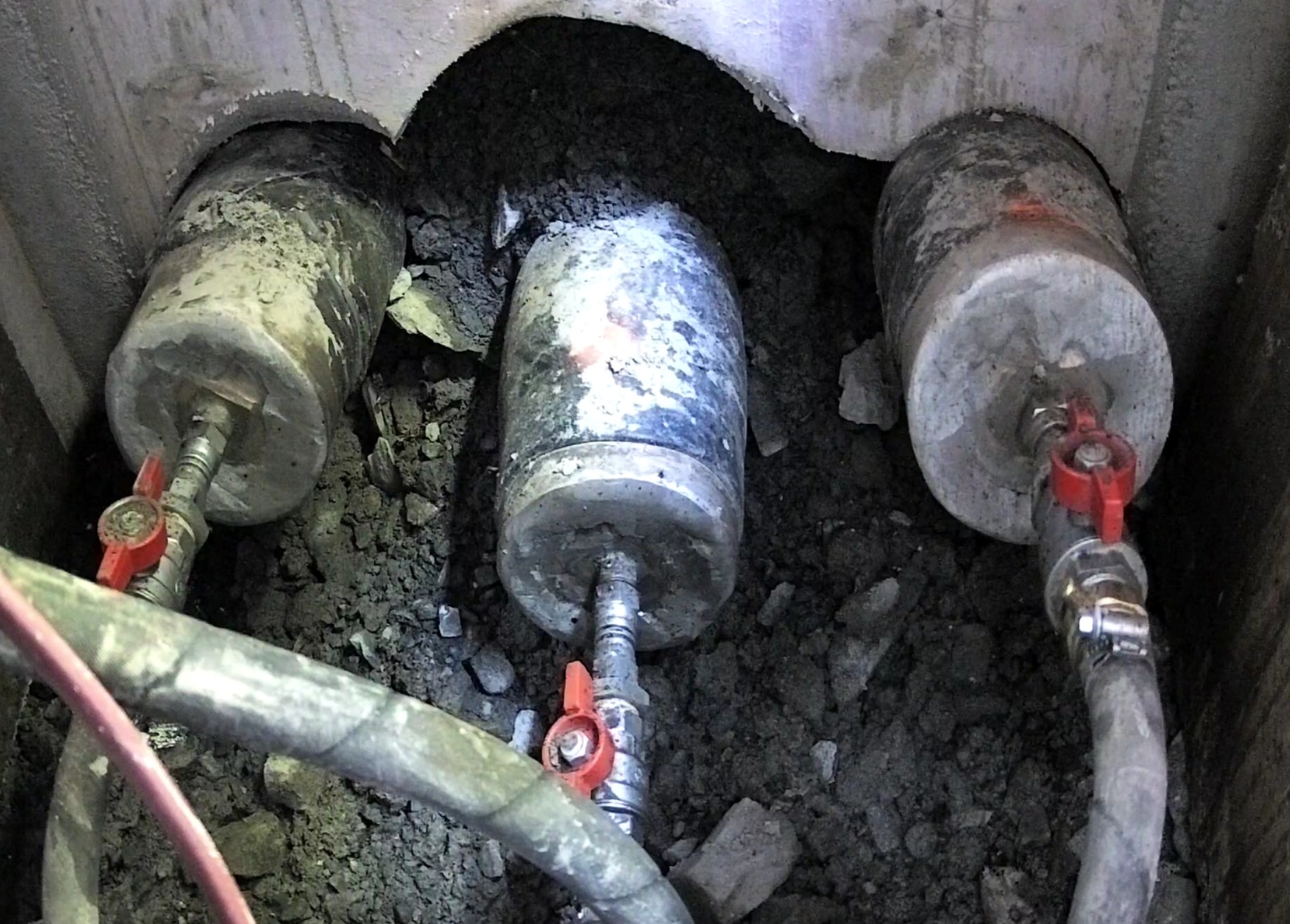 Three sealed oil-filled cable ends in an open jointing pit, fitted with red ball valves and hoses for bacterial circulation
