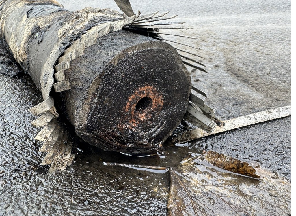 Sectioned 300kV oil-filled power cable lying on wet ground, dielectric oil pooling around the cut end