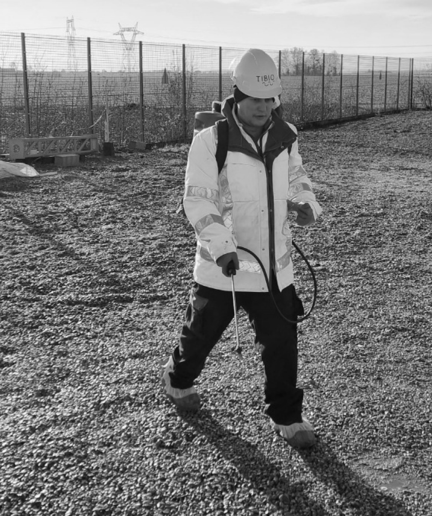 bionrec technician applying bacterial solution by backpack sprayer across a substation gravel surface